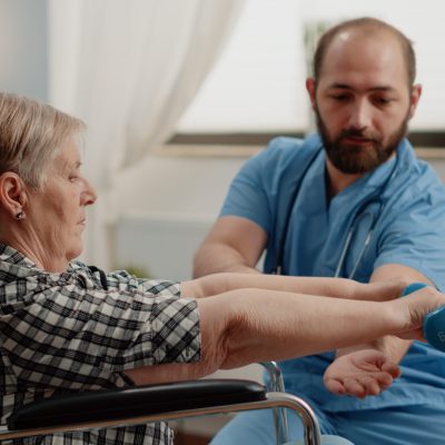 Nurse assisting disabled patient with physical exercises for recovery
